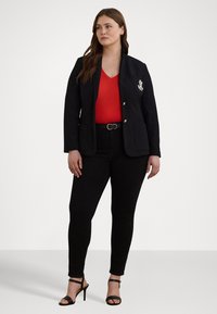 Marineblazer med hvitt emblem, svarte skinny jeans, rød topp og svarte hæler med stropper. Stofdetaljene inkluderer glatt tekstur og tettsittende design.