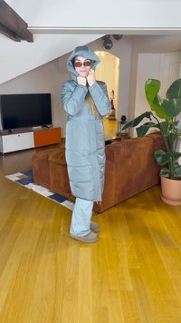 Dlhý svetloblý púderový kabát s kapucňou, stiahnutým pásom a ribovanou textúrou. Skombinovaný so širokými svetloblými džínsami a hnedou obuvou.