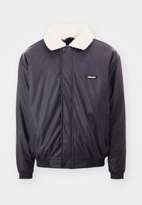 Chaqueta bomber negra con un cuello blanco esponjoso, puños elásticos y cintura ajustable. Presenta un pequeño logo negro en el pecho. Textil suave y brillante.