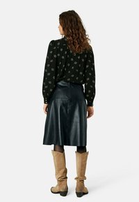 Blusa nera con motivi geometrici, abbinata a una gonna in pelle nera lucida fino al ginocchio e stivali in suede beige alti fino al ginocchio.