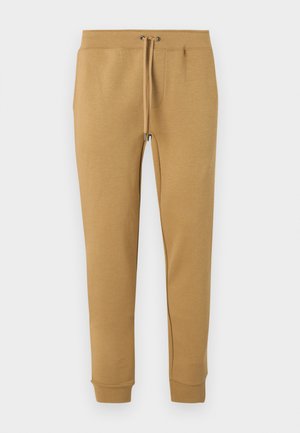 Pantalon de survêtement beige fuselé avec taille élastique et cordon de serrage, chevilles resserrées, présenté sur fond blanc.