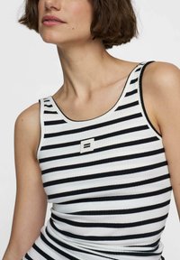 Schwarz-weißer gestreifter Tanktop mit geripptem Textur, versehen mit einem kleinen quadratischen Logo in der Mitte und breiten Schulterträgern.