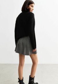 Suéter negro de punto con hombros caídos, combinado con una falda plisada de pata de gallo y botas negras de tobillo con hebillas.