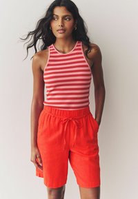 Top con righe rosse e collo alto, abbinato a pantaloni corti in lino rossi larghi con vita elastica e dettaglio con cordoncino.