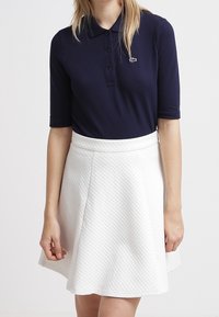 Marinblå polo skort med kort ärm och tre knappar, i kombination med en vit utsvängd kjol som har ett strukturerat mönster och midjeresår.