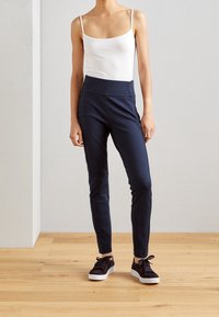 Pantalons navy ajustés avec une taille haute, fabriqués dans un tissu lisse. Associés à un débardeur blanc et des baskets noires avec des semelles blanches.