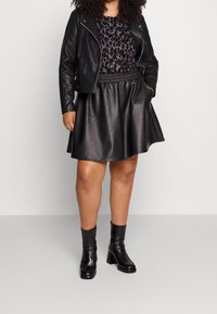 Veste de motard en cuir noir, haut à imprimé léopard et jupe trapèze en similicuir noir associée à des bottines à talons noires.