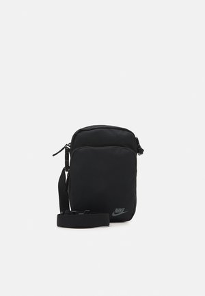 Petit sac bandoulière noir Nike avec sangle réglable, fermetures éclair et poche avant, présenté sur un fond clair uni.