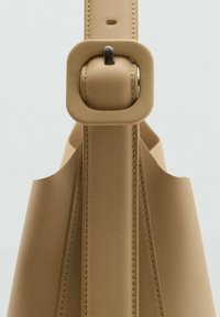 Borsa a tracolla in pelle beige con una fibbia quadrata su una larga cinghia, design senza cuciture e cuciture a vista lungo i bordi.