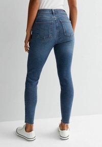 Högmidjade, slim fit jeans i medelblå denim. Har fransade fållar, två bakfickor och en slät, strukturerad yta.