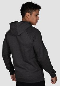 Dunkelgrauer Hoodie aus strukturiertem Stoff, mit einer Kängurutasche, Kapuze mit Kordelzug und einem schwarzen Patch am linken Ärmel.
