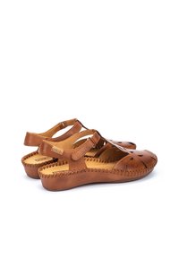 Sandali in pelle marrone con motivi intagliati, cinturini regolabili e cuciture текстurate. Suola piatta con leggero tacco rialzato per il massimo comfort.