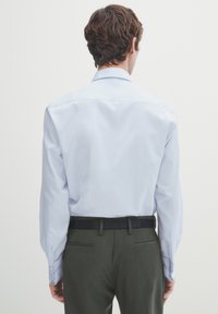 Himmelblaues Langarmhemd mit spitzem Kragen und Knopfmanschetten, kombiniert mit dunkelgrünen Hosen und einem schwarzen Gürtel. Glatte Stofftextur.