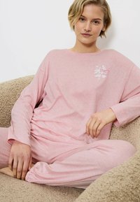 Set aus weichem, hellrosa Loungewear. Das langärmlige Oberteil hat ein florales Design. Die Hose hat einen elastischen Bund und tapered Beine.