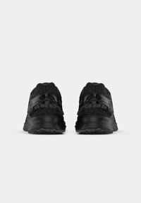 Chaussures de sport noires avec tissu texturé, accents réfléchissants et un collier rembourré. Semelles épaisses offrant amorti et soutien.