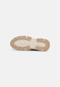 Schuhsohle aus beigem Gummi; weist eine strukturierte, gemusterte Oberfläche mit mehreren Grip-Punkten und Konturen für besseren Halt auf.