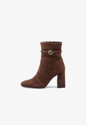 Brune suedestøvle til anklen med en spids tå, indwrapped rem og rund spænde-detail, hævet blokhæl og glat overflade.