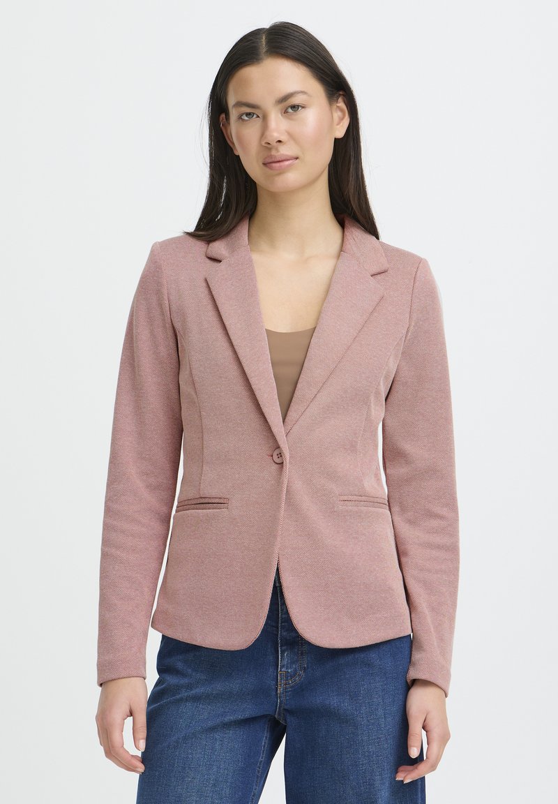 Blazer rosa texturizado con solapas con muesca, cierre de un botón y dos bolsillos delanteros. Combinado con una camiseta beige y jeans azul oscuro.
