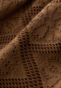 Materialul tricotat de culoare maro are o textură complexă, cu modele intricate, prezentând desene cu goluri și diverse texturi în întreaga sa suprafață.