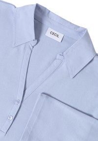 Jasnoniebieska bluzka z klasycznym kołnierzykiem, zapięciem na guziki i kieszonką naszywaną. Wykonana z miękkiego materiału, z delikatnymi detalami haftu.