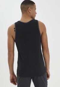 Top da allenamento nero con bordi grigi, scollatura rotonda e design aderente. Presenta uno stile racerback e una texture liscia simile al cotone.