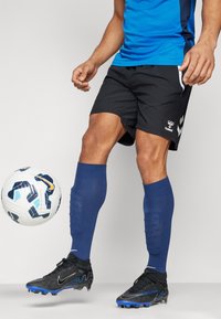 Fekete short, kék sportpóló, kék térdmagasságú zoknik, fekete és kék focicipők, valamint egy fehér és kék foci labda mozgásban.