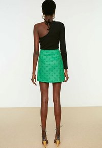 Mustat topit yhdellä olalla, jossa on solmuseikka; vihreä mini-hame kukkakuviolla; nilkkaketjulliset korkokengät; näkyy takaa.