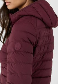 Giacca a vento bordeaux con cappuccio, con texture trapuntata e una patch in gomma sul maniche. Design leggero e isolato.