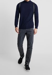 Námořnický pletený svetřík s vysokým límcem, kombinovaný s tmavě šedými slim-fit kalhotami a černými teniskami. Minimalistický design a měkká textura.