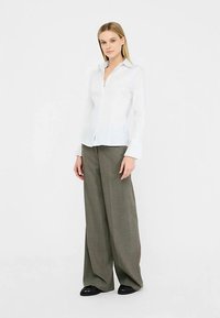 Biała koszula na długi rękaw z guzikami i kołnierzykiem, zestawiona z szerokimi, oliwkowozielonymi spodniami o subtelnej fakturze oraz ciemnymi butami.