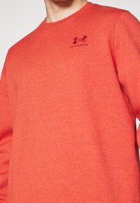 Sudadera roja hecha de tela suave, con cuello redondo, mangas largas y un pequeño logotipo negro en la parte superior izquierda del pecho.