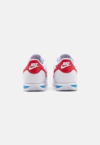 Nike sneakers med en hvid base, røde accenter og en lyseblå ydersål. Glat læder og mesh-materialer med polstrede kraver.