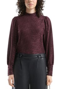 Bordowa fakturowana bluzka z długimi bufkami, wysokim kołnierzem i subtelnym kwiatowym wzorem, zestawiona z czarnymi, skórzanymi spodniami z wysokim stanem.