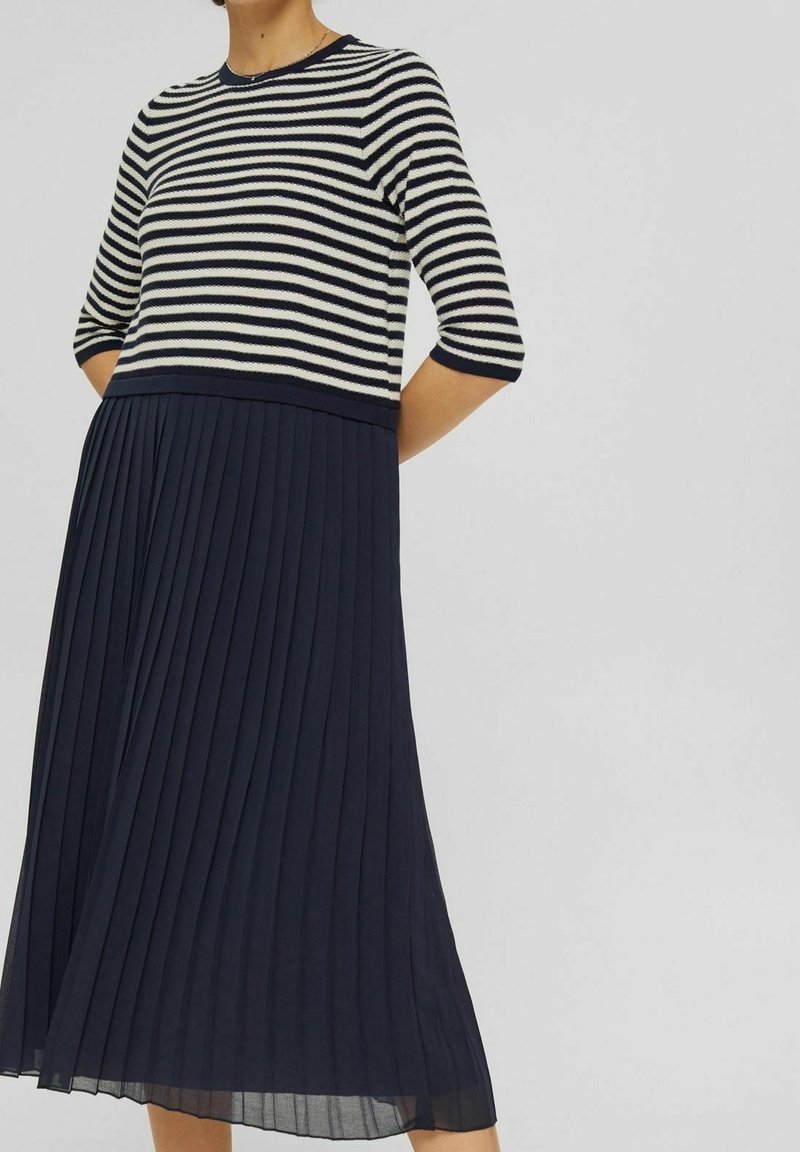 Randig stickad klänning med korta ärmar, som har en figurnära överdel i marinblått och vitt, som övergår till en plisserad marinblå kjol.