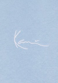 Lys blå strikket stoff med en glatt tekstur, med et hvitt brodert signaturdesign i kursiv.