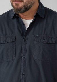 Donkerblauwe button-up shirt gemaakt van lichtgewicht stof; heeft twee voorkruisen, een zachte textuur en een puntige kraag.