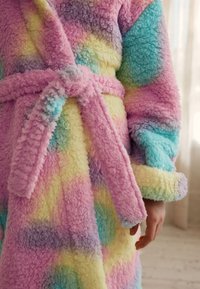 Peignoir en tissu pelucheux avec des couleurs pastel : rose, bleu, jaune et violet. Texture douce, design ceinturé, avec de larges poignets et une allure confortable.
