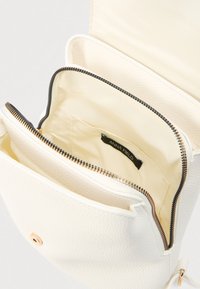 Λευκή τσάντα χειρός από υφή δέρματος με φερμουάρ κλεισίματος, διαθέτει λείο εσωτερικό και εσωτερική τσέπη με την ετικέτα "ANNA FIELD".