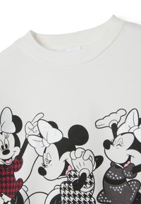Sweatshirt blanc orné de personnages illustrés noirs et rouges avec des accents en noeud, des motifs pied-de-poule et des détails brillants sur une texture douce.