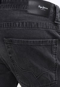 Jeans de mezclilla negros con un bolsillo trasero que presenta un diseño de costura en forma de V y una etiqueta de leather etiquetada "Pepe Jeans London". Tejido texturizado.