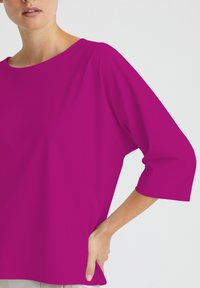 Fuchsia übergroße Bluse mit weitem Ausschnitt und Dreiviertelärmeln, aus glattem Stoff gefertigt, mit einer lockeren Passform und Seitenstecktasche.