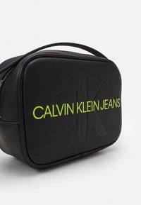 Czarna torba z faux skóry o prostokątnym kształcie. Na przedniej części znajduje się wytłoczone logo "CK" oraz "CALVIN KLEIN JEANS" w jasnoszonym kolorze.