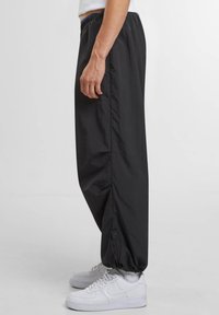 Zwarte, lichtgewicht nylon broek met een loszittende pasvorm, elastische tailleband en verstelbare enkelboorden, gecombineerd met witte sneakers.