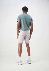 Shorts gris clair avec des ourlets roulés, associés à un t-shirt vert foncé. Tissu flexible, manches courtes, et baskets de sport complètent la tenue.