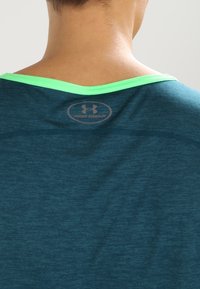 Teal skjorta med grön halsringning, med en Under Armour-logotyp på baksidan. Tyget ser texturerat och lätt ut.