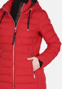 Chaqueta acolchada roja con cierre de cremallera, capucha y dos bolsillos laterales. Tiene una textura acolchada y cordones y forro en negro contrastante.