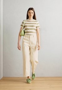 T-shirt à manches courtes rayé en beige et olive, pantalon taille haute beige et chaussures à lacets vert clair. Accessoire de sac à main vert.