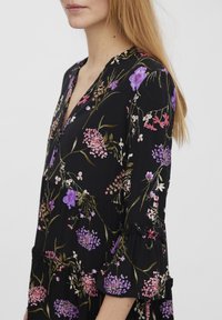 Mustapuku, jossa on kukkakuosi, joka sisältää violetteja, vaaleanpunaisia ja valkoisia kukkia. Siinä on V-kaula-aukko ja röyhelökoristeiset kolmisen neljäsosapituista hihoista.