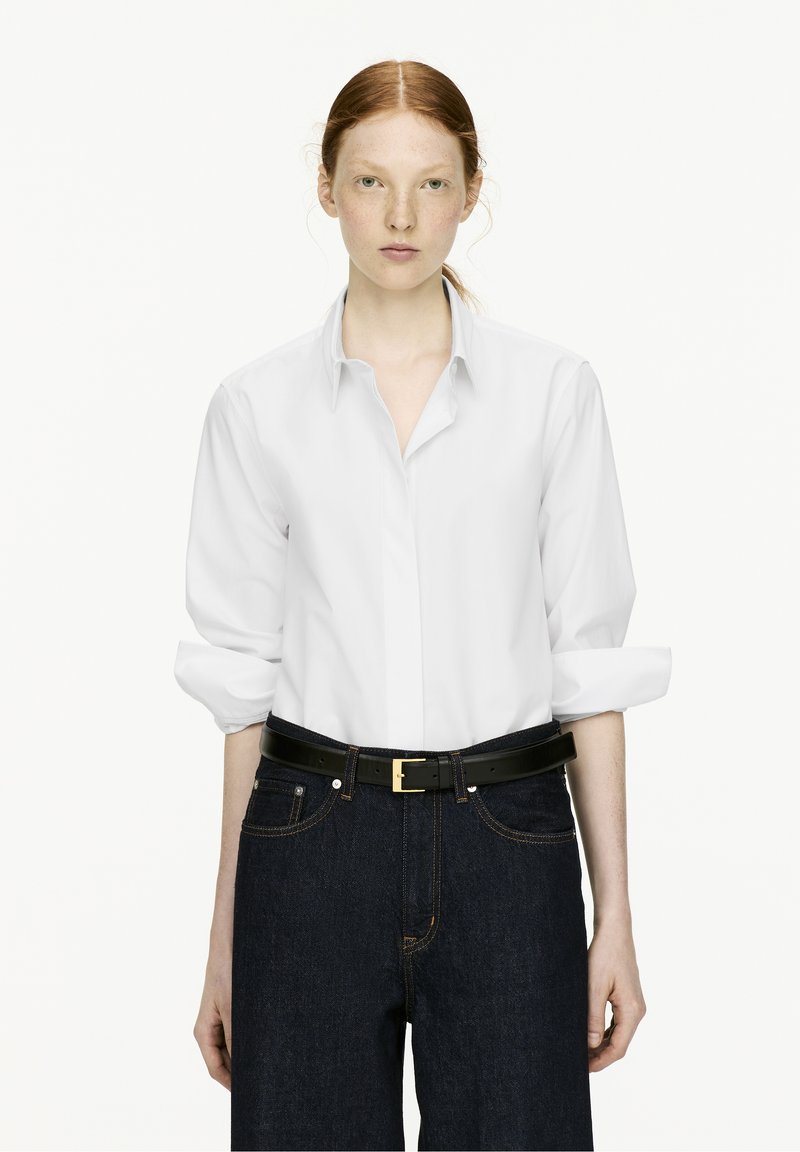 White long-sleeve button-up shirt with rolled sleeves, paired with dark denim high-waisted jeans and a black belt featuring a gold buckle.