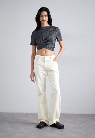 Γκρι κοντό μπλουζάκι με κοντά μανίκια και λεπτομέρειες υφής, σε συνδυασμό με κρεμ παντελόνι με φαρδύ παντελόνι. Μαύρα παπούτσια με κίτρινο λογότυπο στο μπροστινό μέρος.